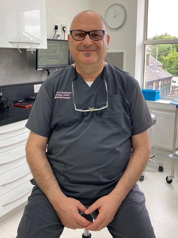 Dr Stavros, sitting on a stool in the Vermilion surgery in Edinburgh