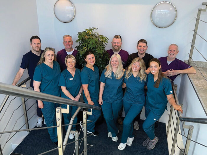 Five men and six women pose in a stairwell wearing dental scrubs.